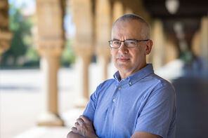 Matthew Sommer wearing a light-blue collared shirt standing under one of arcades on Stanford's Main Quad