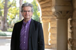 Nicholas Jenkins wearing a purple button-down shirt and a black sport coat standing under one of Stanford's arches in the Main Quad.