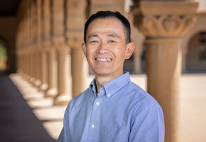 Tadashi Fukami wearing a light-blue collard shirt standing under the arcades along Stanford's Main Quad