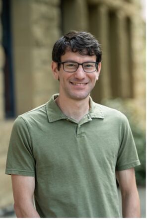 Ben Feldman with short dark hair and glasses in a moss-green polo shirt