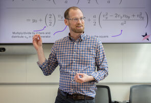 Ben Lev explains with his hands in front of a slide displaying a physics equation