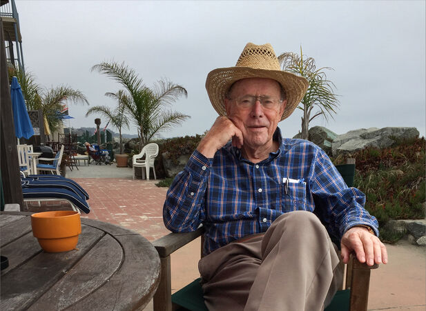 Image of Walter A. Harrison sitting in a chair at a beach with palm trees in the background. 