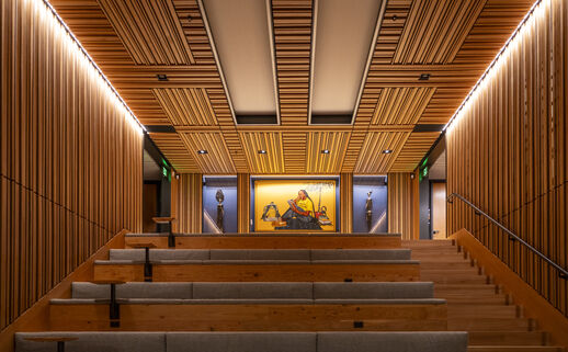 Wooden stadium seating leads up to painting covered by a wood-slat ceiling