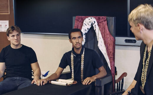 Two seated students look intensely at a speaker as they perform Richard III