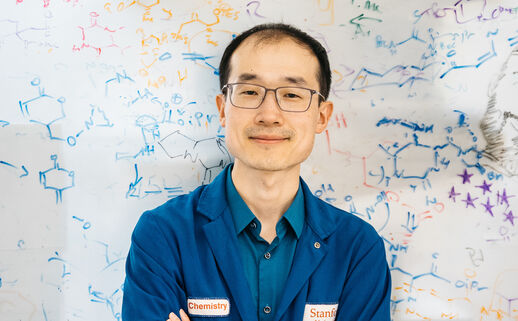 Song Ling wears a blue lab coat and stands in front of a whiteboard filled with drawings of organic molecules