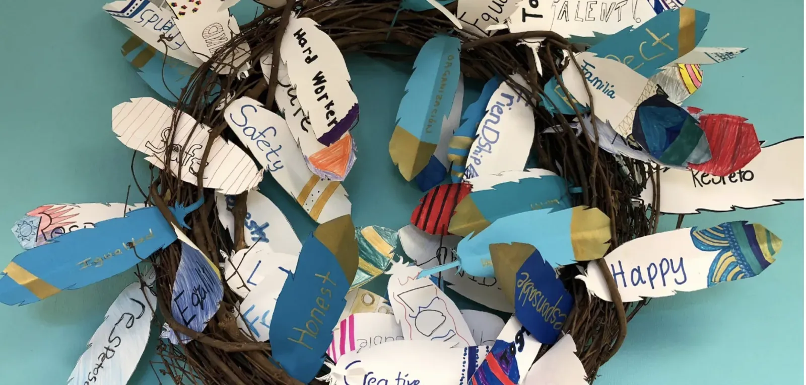 Image of a wreath with paper feathers on it. The paper feathers have writing on them that represent the values that each student's family cherishes.