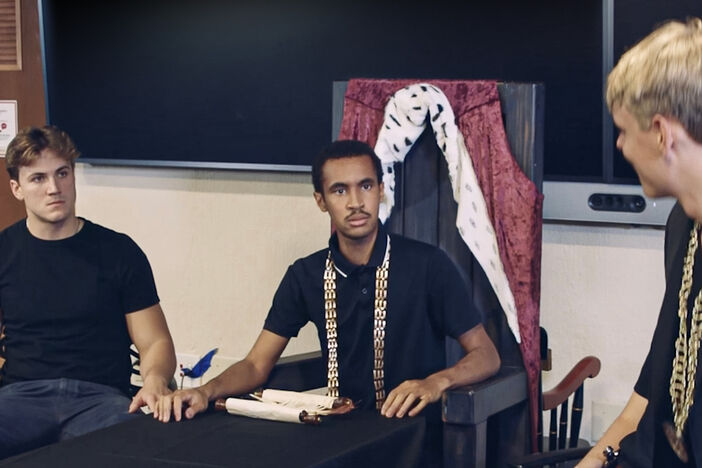 Two seated students look intensely at a speaker as they perform Richard III
