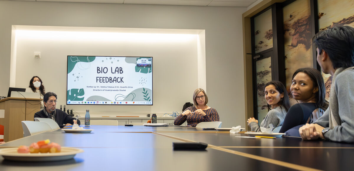Professors and students sit around a conference room table and look at one student who is speaking.