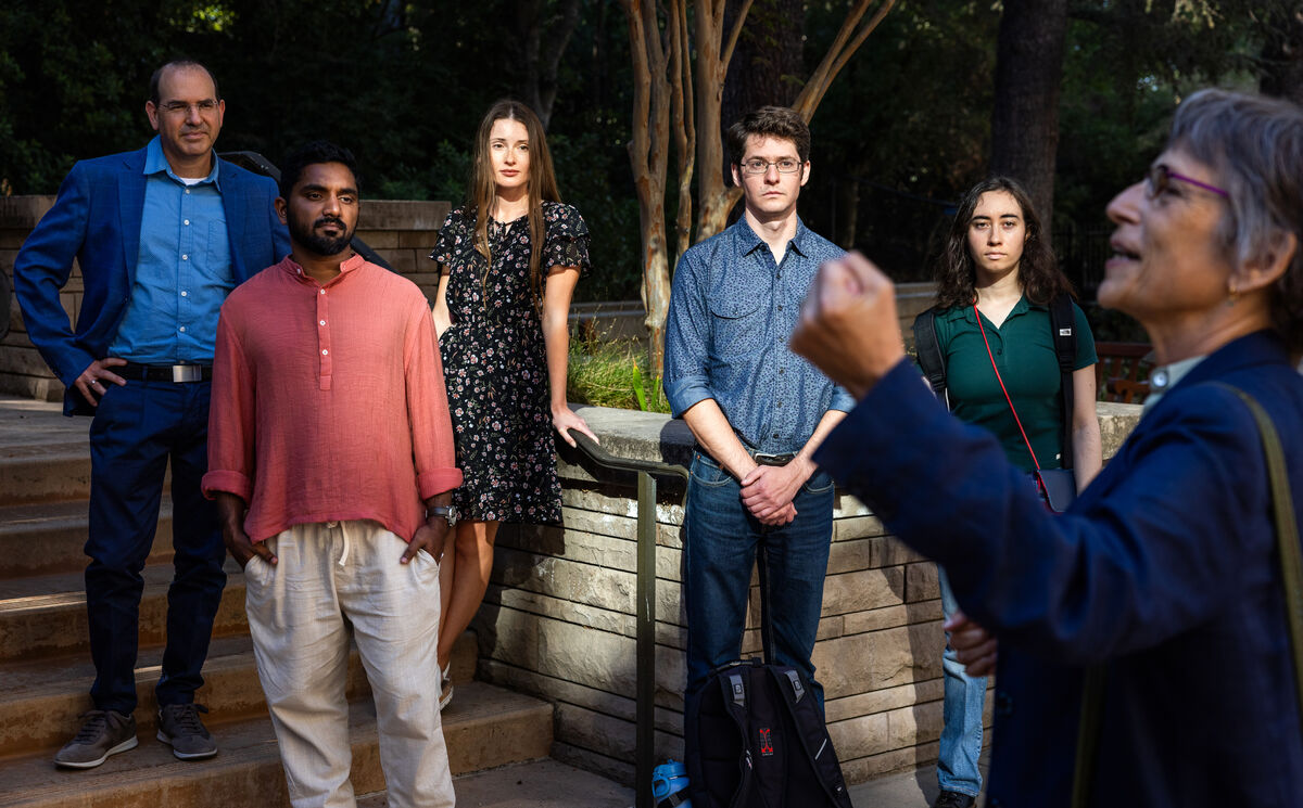 Debra Satz in the foreground, speaking with a raised fist, while a group of scholars listen