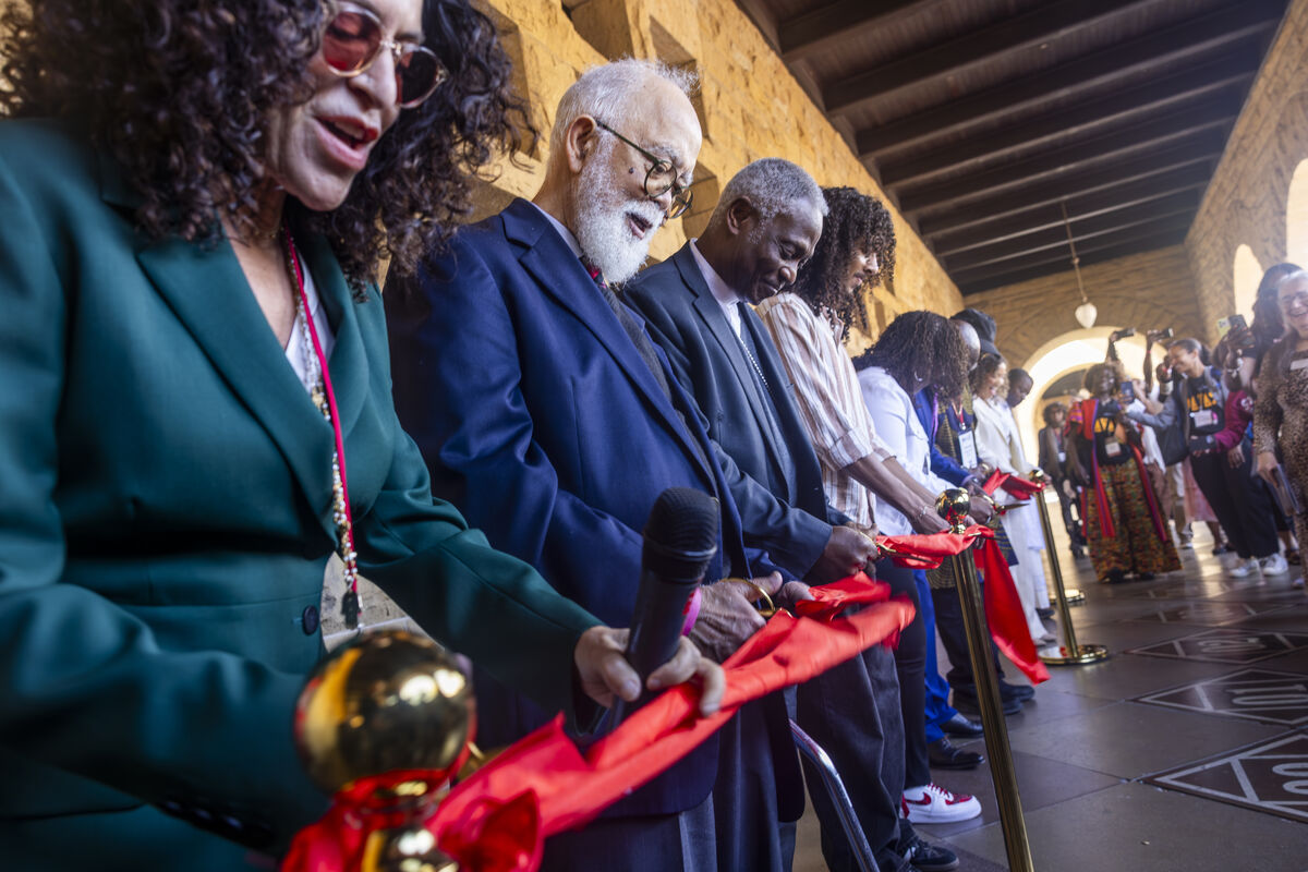 Black adults stand shoulder to shoulder and cut a long red ribbon