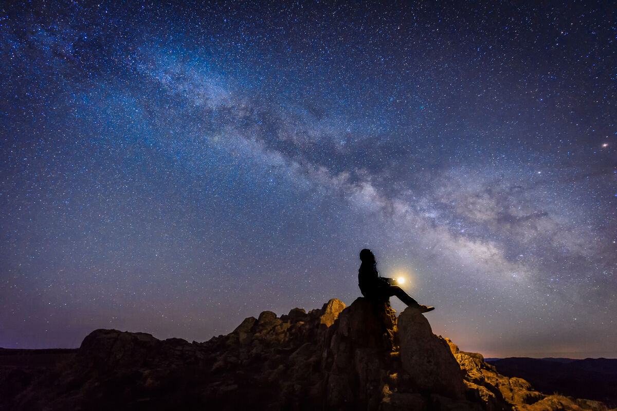 Person sitting on rocks looking up at the Milky Way