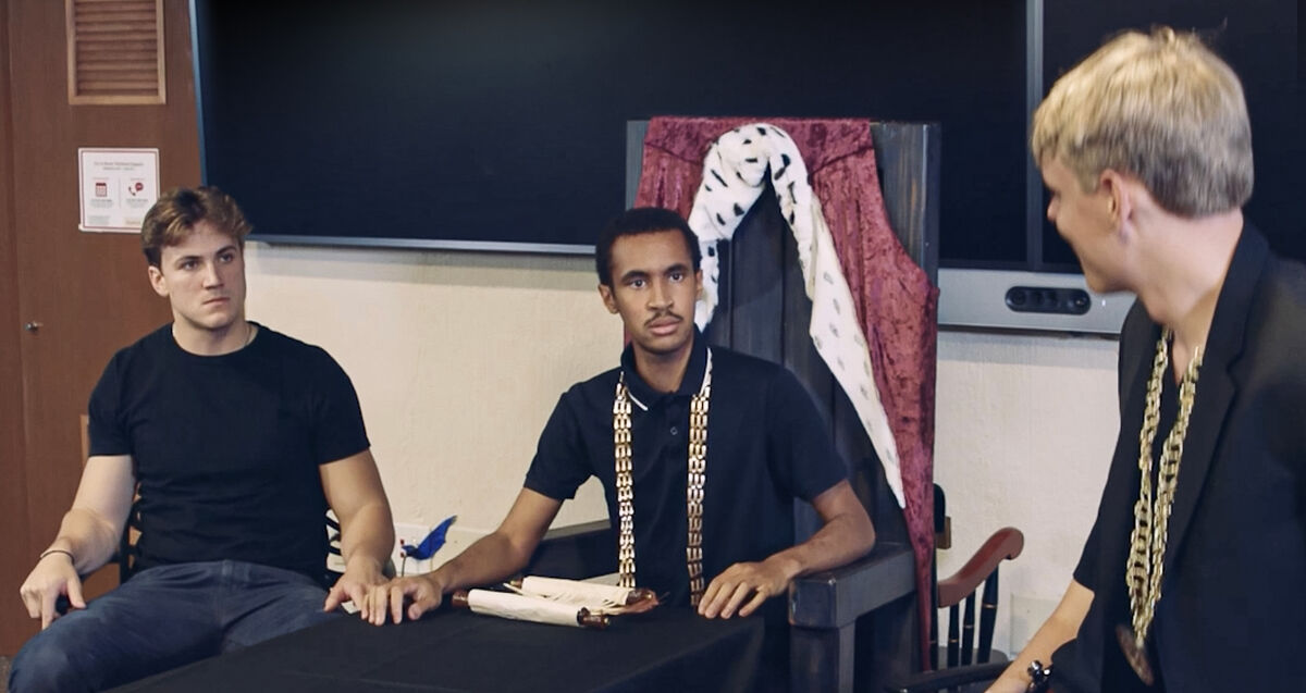 Two seated students look intensely at a speaker as they perform Richard III