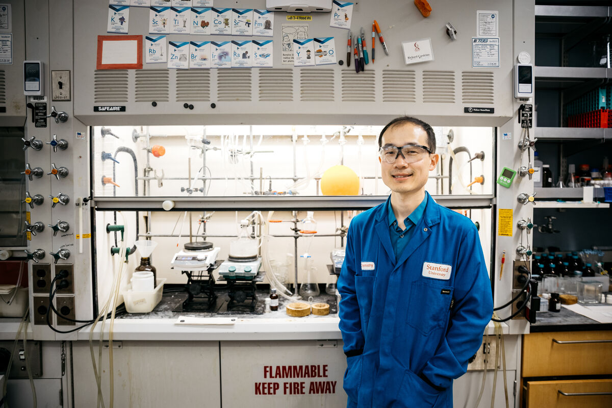Song Lin stands in his lab wearing safety goggles and a blue lab coat