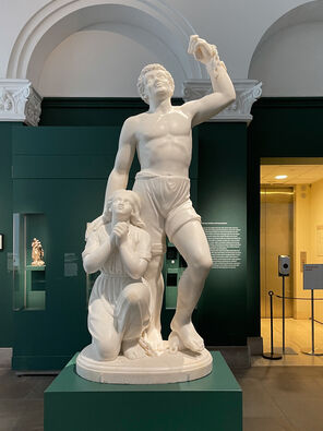 Photo of a white marble sculpture of two figures: a female kneeling and a man standing with a raised fist and a broken manacle