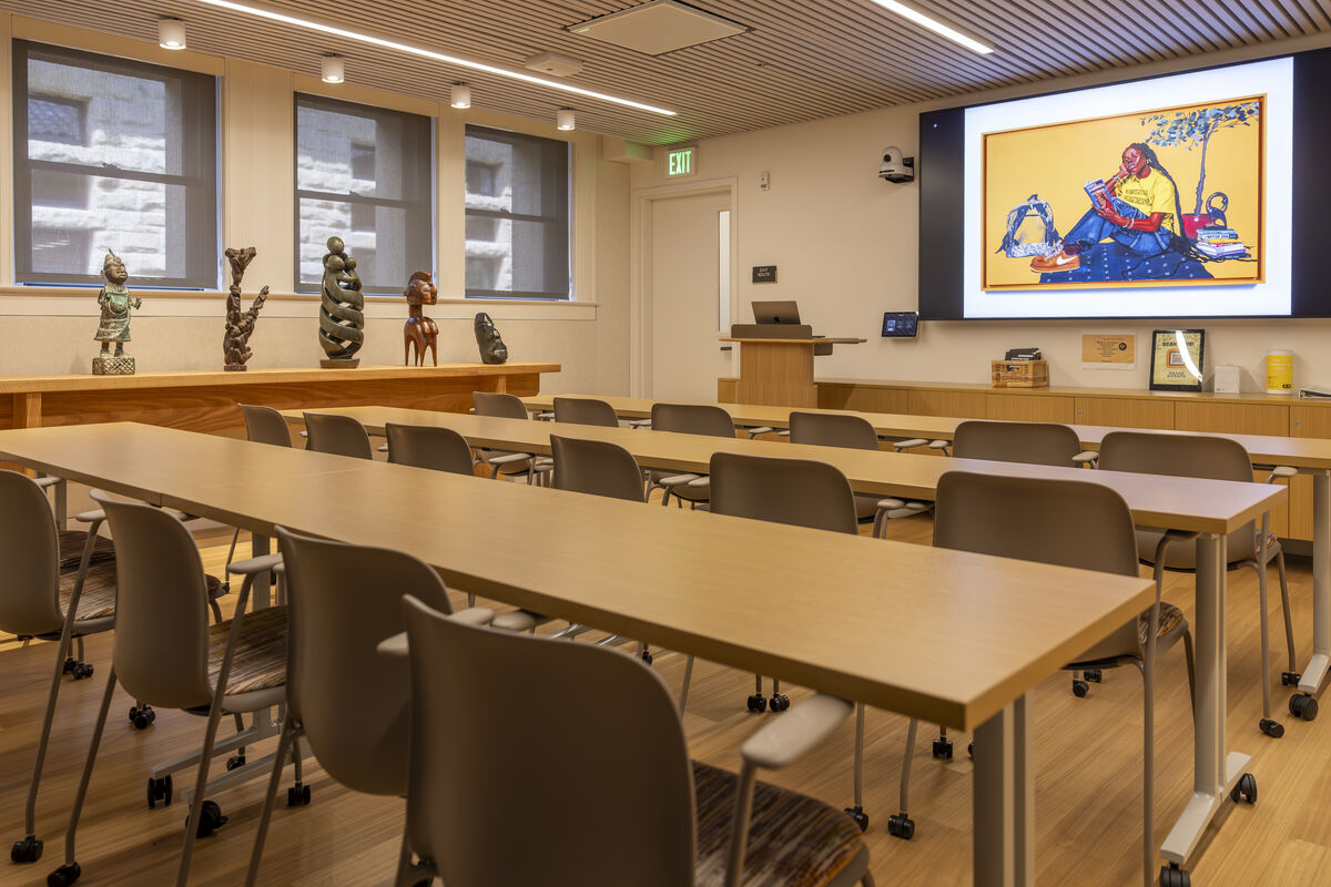 A room with rows of long tables and chairs with a side table displaying small sculptures