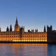 Big Ben and Westminster Palace, both lit up at dusk, seen from across River Thames.