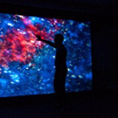 Silhouette of a person standing in front of a lit image of outer space.