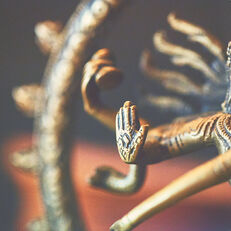 A close-up of a brass figure, representing a deity, with their arm extended forward, palm facing out