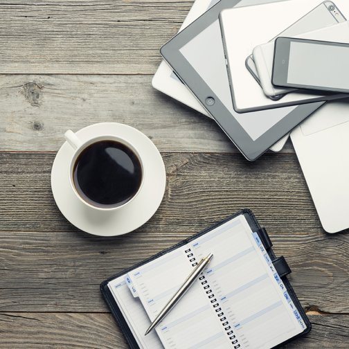 A cup of coffee, notebook and mobile devices sitting on a table.