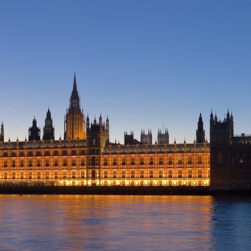 Big Ben and Westminster Palace, both lit up at dusk, seen from across River Thames.