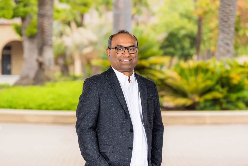 Sourav Chatterjee wearing a white collared shirt and a black sport coat and standing in Stanford's Main Quad