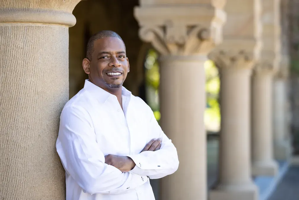 A. Van Jordan wearing a white button-down shirt and leaning against one of the columns of Stanford University's Main Quad