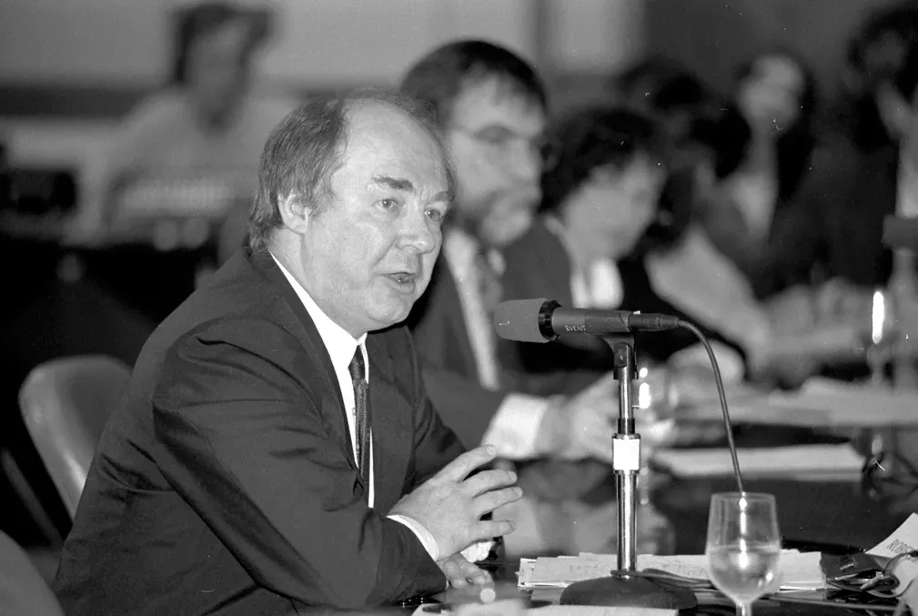 Black and white photo of Robert Packenham speaking into a microphone