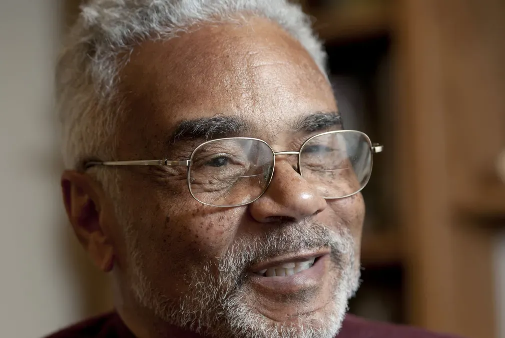 Photo of Clayborne Carson with a gray mustache and short beard, wearing glasses and a dark-red sweater