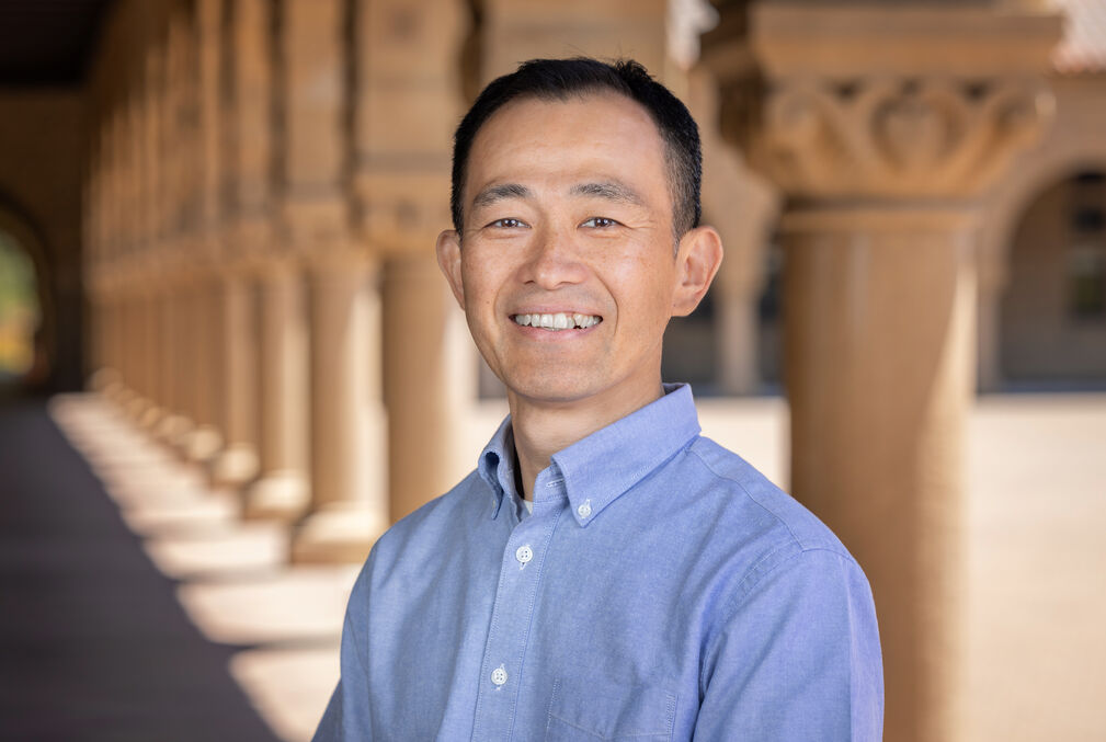 Tadashi Fukami wearing a light-blue collard shirt standing under the arcades along Stanford's Main Quad