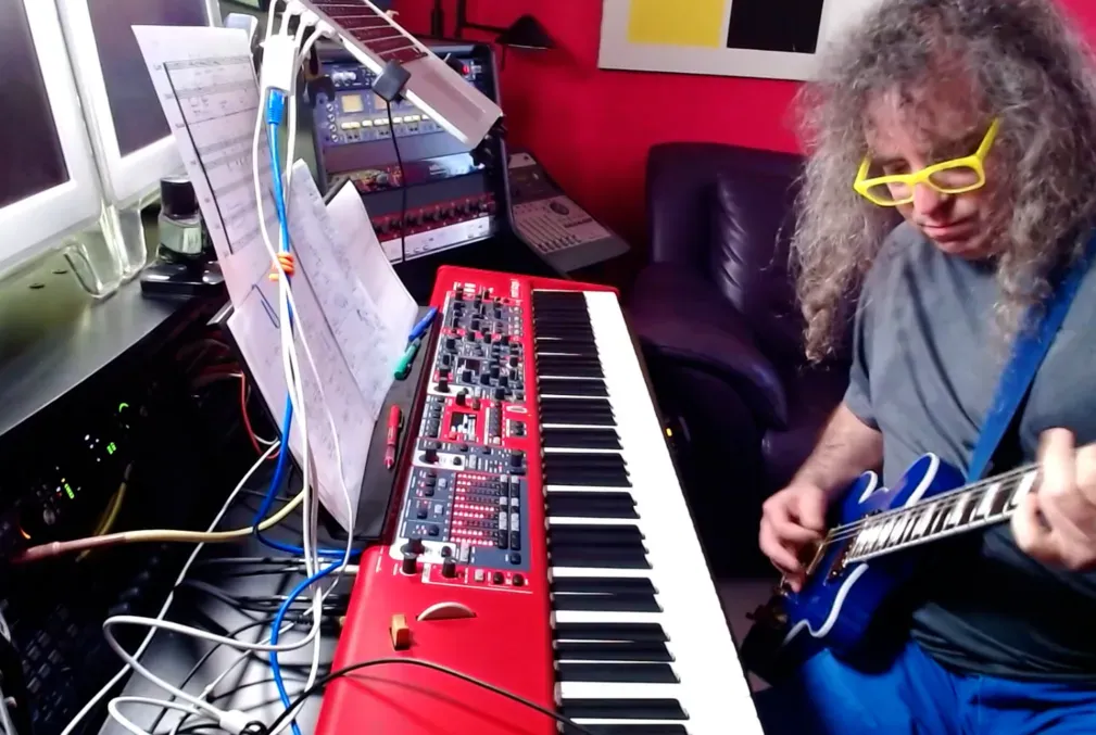 Mark Applebaum plays guitar while sitting at keyboard