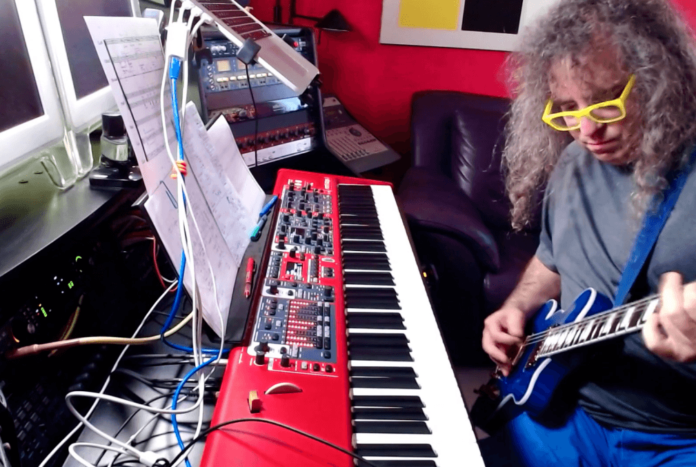 Mark Applebaum plays guitar while sitting at keyboard