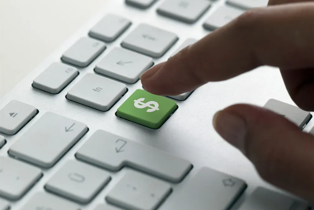 An index finger hovers above an all-green key bearing a dollar sign that is part of an otherwise white keyboard