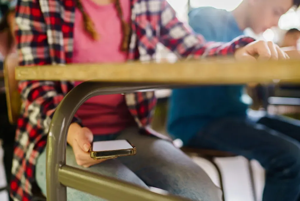 A student holds a phone underneath a desk to sneak a look at it.