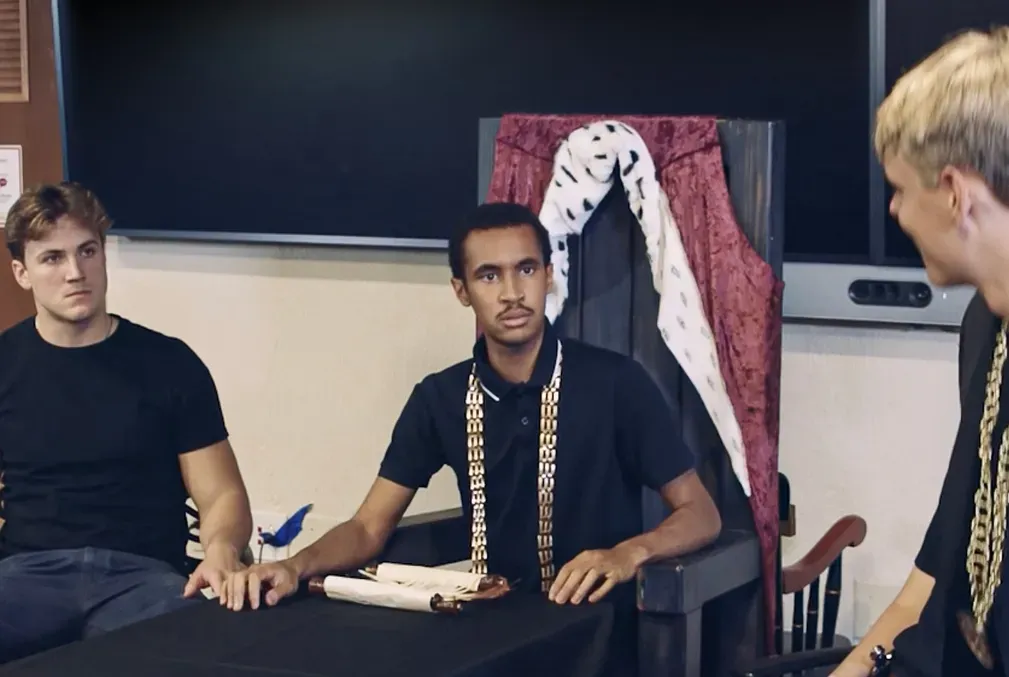 Two seated students look intensely at a speaker as they perform Richard III