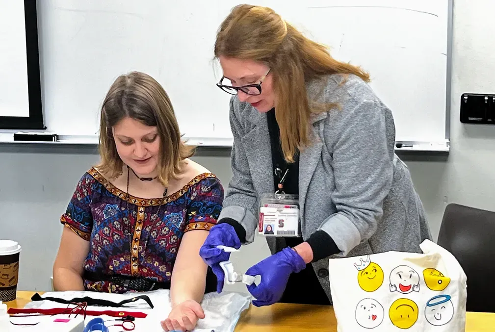 A young woman holds out her arm for a gloved medical professional to swab it for a sweat test.