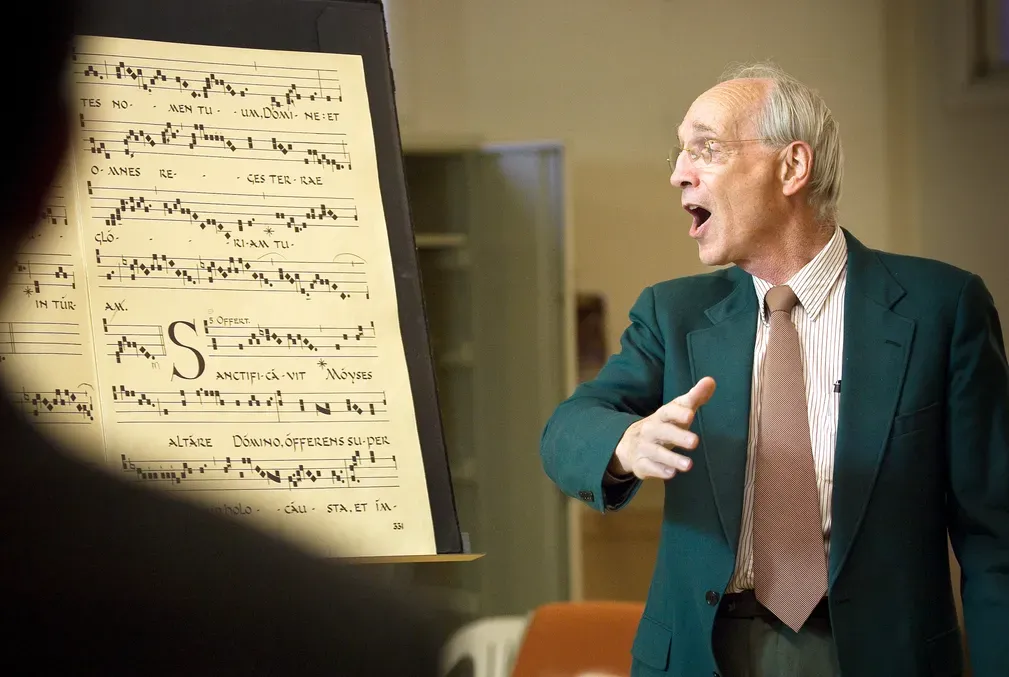 Photo of Bill Mahrt singing and looking to the left as Gregorian Chant is written out behind him